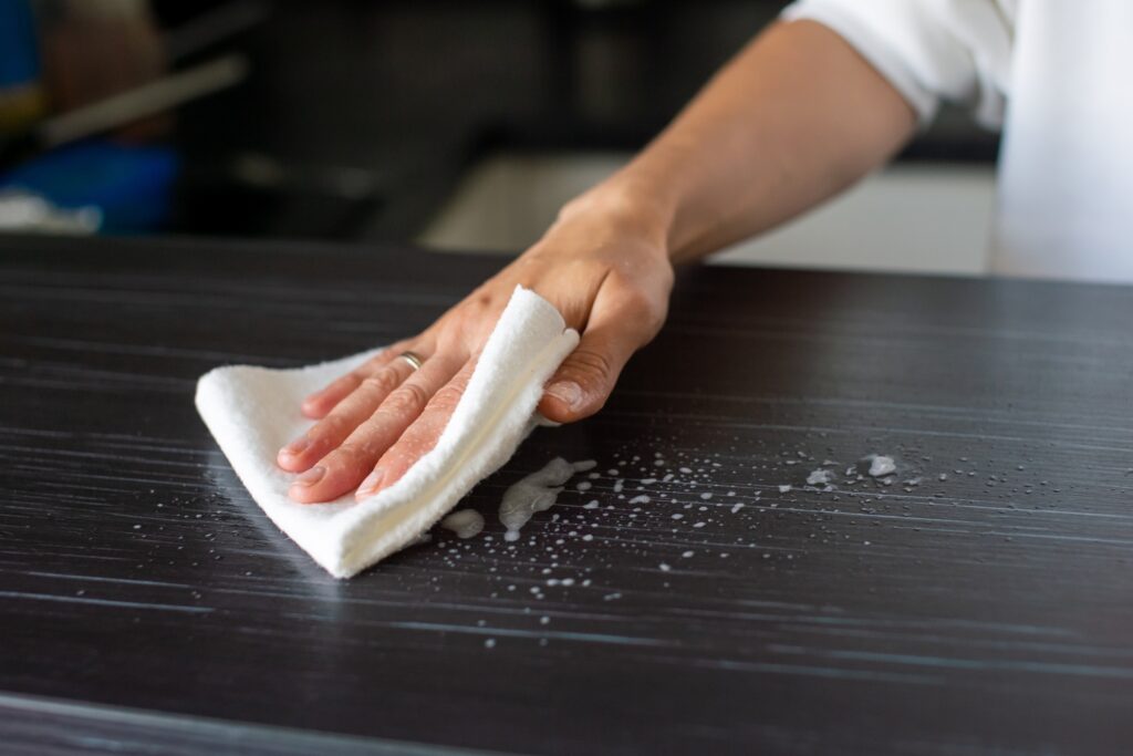 Hand wiping dark kitchen benchtop with white cloth removing soapy residue and water droplets